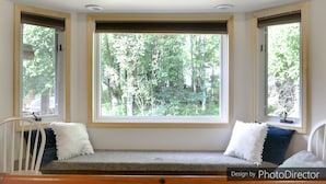 Une grande fenêtre en saillie donnant sur les arbres, un banc agrémenté de coussins et des tableaux encadrés accrochés au mur.