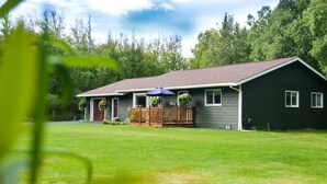 Une maison à deux étages avec un porche à l’avant, une terrasse en bois et une pelouse.