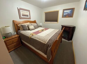 A neatly arranged bedroom with a bed, bedside tables, a lamp, and framed pictures on the walls.
