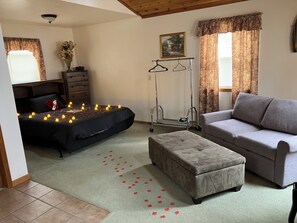 Quarto com cama, sofá cinza, cómoda de madeira, cabideiro e um quadro na parede.