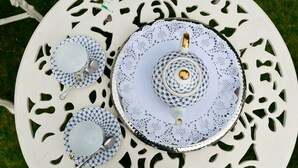 Uma mesa branca ao ar livre com toalha de renda e um conjunto de chá.