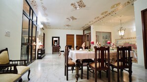 Uma sala de jantar com piso de mármore, cadeiras de madeira, uma mesa posta para quatro pessoas e um lustre.