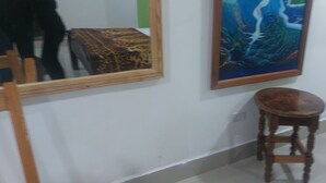A room with a mirror, a painting, and a wooden stool.