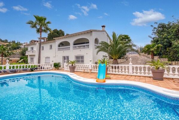 Una piscina con tobogán, un edificio blanco con arcos y palmeras.