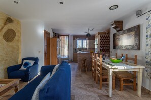 Ein Wohnzimmer mit einer Couch, einem Esstisch mit Stühlen, einer Küchenzeile inklusive Spüle und Arbeitsplatte sowie einem Holzkasten.