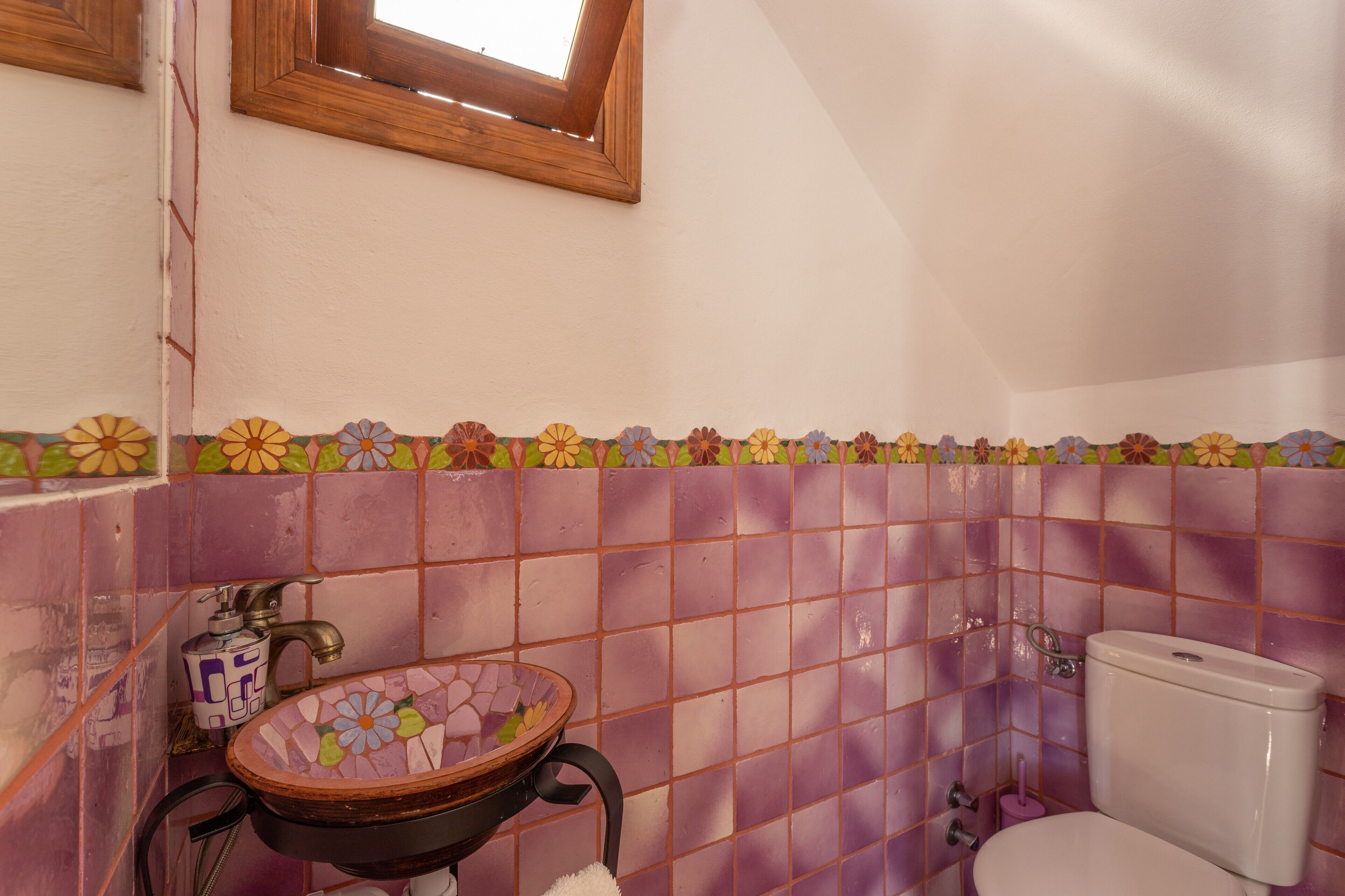 A bathroom with a tiled wall, a sink with a decorative basin, a toilet, and a window above the sink.