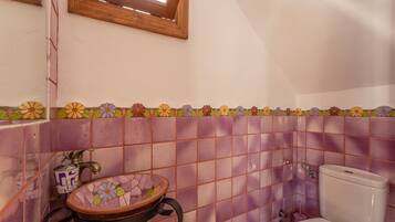 A bathroom with a tiled wall, a sink with a decorative basin, a toilet, and a window above the sink.