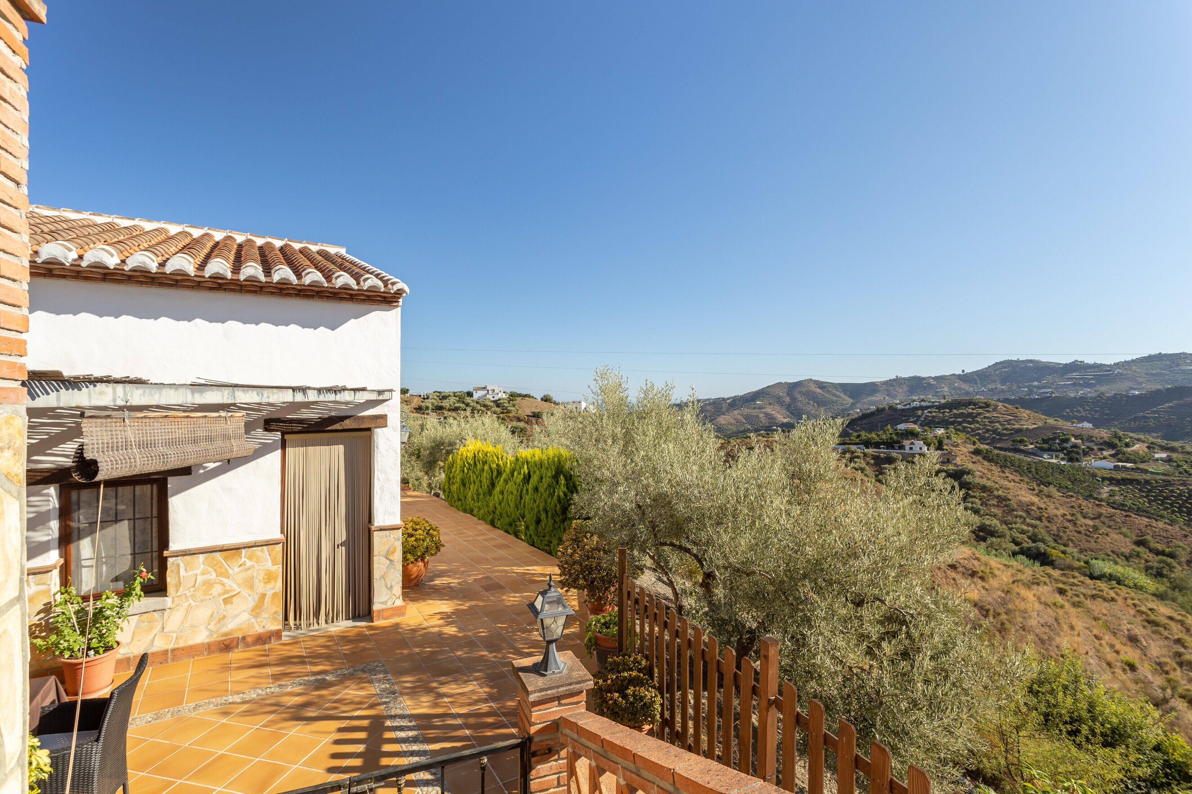 Un balcón con vistas a un paisaje montañoso, un patio con baldosas y una valla de madera.