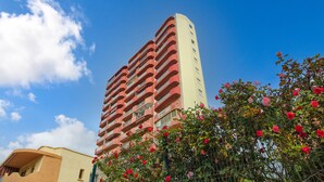 A tall building with balconies, surrounded by a fence with red flowers. - Apartment La Perla Seaview Calpe with Sea View, Pool, Wi-Fi, Air Conditioning, Balcony & Terrace (Calpe)