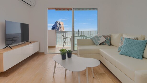 A modern living room with a flat-screen TV, a white coffee table, a beige sofa with patterned cushions, and a balcony with a view of a rocky outcrop. - Apartment La Perla Seaview Calpe with Sea View, Pool, Wi-Fi, Air Conditioning, Balcony & Terrace (Calpe)