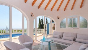 A spacious balcony with a sofa, chairs, and a table, overlooking a pool and greenery. - Casa La Perla: Villa with Sea View, Pool, Balcony, A/C & Wi-Fi (Benitachell)