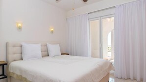 A bedroom with a large bed, two bedside tables, a ceiling fan, and a sliding glass door leading to an outdoor area. - Casa La Perla: Villa with Sea View, Pool, Balcony, A/C & Wi-Fi (Benitachell)