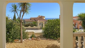 A building with a tiled roof, surrounded by greenery and a clear view of the sea. - Casa La Perla: Villa with Sea View, Pool, Balcony, A/C & Wi-Fi (Benitachell)