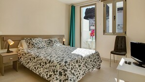 A bedroom with a bed, a desk, a chair, a TV, and a window with curtains.
