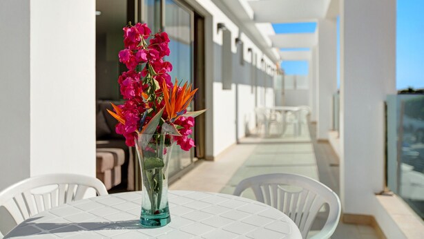 A balcony with a table, chairs, and a vase of flowers.