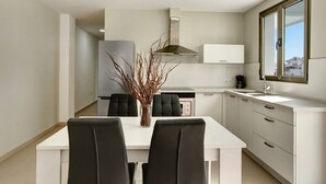 A modern kitchen with white cabinets, a stainless steel range hood, and a dining area with a white table and black chairs.