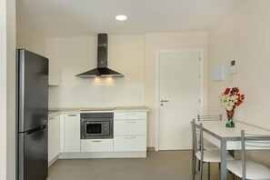 A compact kitchen with a refrigerator, oven, microwave, and a stainless steel range hood.
