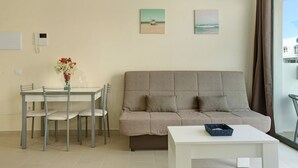 A living room with a sofa, dining table, chairs, and a vase of flowers. - Apartment Albamar 1D with Mountain View, Wi-Fi, A/C & Balcony (Puerto de Mogán)
