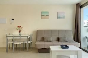 A living room with a sofa, dining table, chairs, and a vase of flowers.