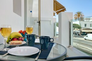 Une table avec une assiette, deux verres de vin, une banane, des raisins et une tasse sur un balcon donnant sur une rue.
