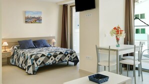 A hotel room with a bed, a desk, a chair, a TV, and a painting on the wall. -  Apartment Albamar 1A with Mountain View, Wi-Fi, A/C, Balcony & Terrace (Puerto de Mogán)