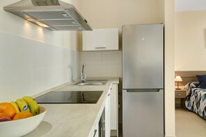Een compacte keuken met een roestvrijstalen koelkast, een fruitschaal op het aanrecht en een klein spoelbakje.