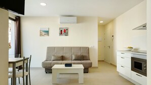 A modern living room with a sofa, a dining table, and chairs. There is a kitchen area with cabinets and an oven. -  Apartment Albamar 1A with Mountain View, Wi-Fi, A/C, Balcony & Terrace (Puerto de Mogán)