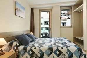Hotelkamer met een bed, nachtkastje, lamp, schilderij aan de muur en uitzicht door een open deur.