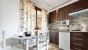 A compact kitchen with a white table, a white chair, a white refrigerator, and dark wooden cabinets. - Vacation Home 'El Lagar' with Mountain View, Shared Terrace and Wi-Fi (Los Silos)