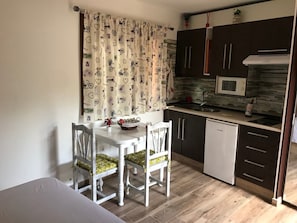 Cozinha compacta com mesa de jantar, cadeiras, micro-ondas e um frigorífico pequeno.