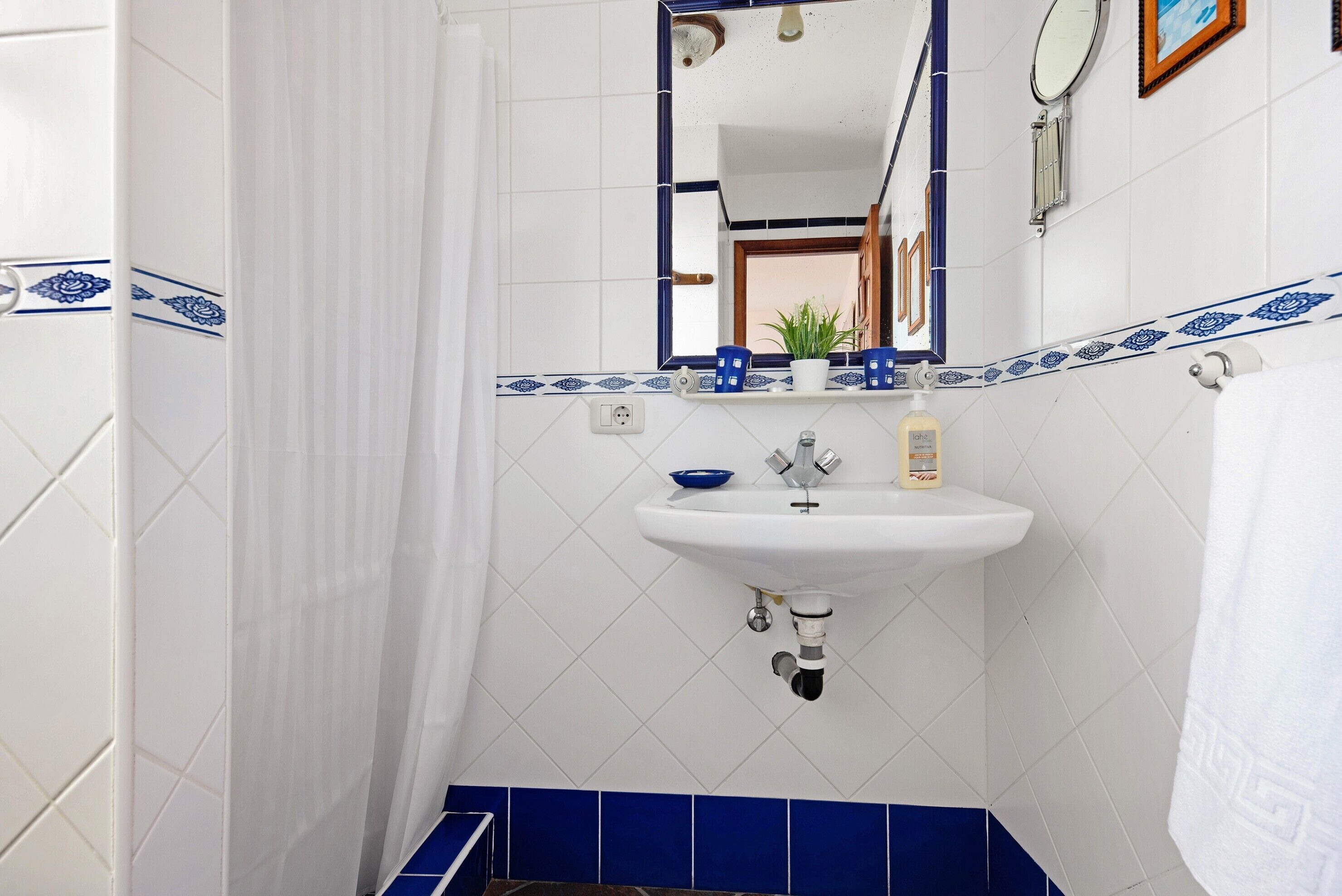 A bathroom with a white sink, blue tiles, a mirror, and a shower curtain.