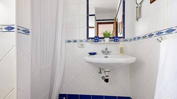 A bathroom with a white sink, blue tiles, a mirror, and a shower curtain.