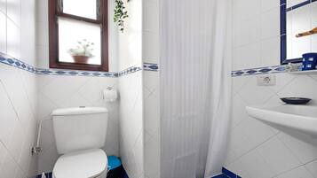 Een badkamer met toilet, douchegordijn, wastafel en een raam met plant.