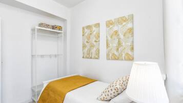 Een slaapkamer met een bed, een witte lamp, een plank met decoratieve objecten en twee kunstwerken aan de muur.