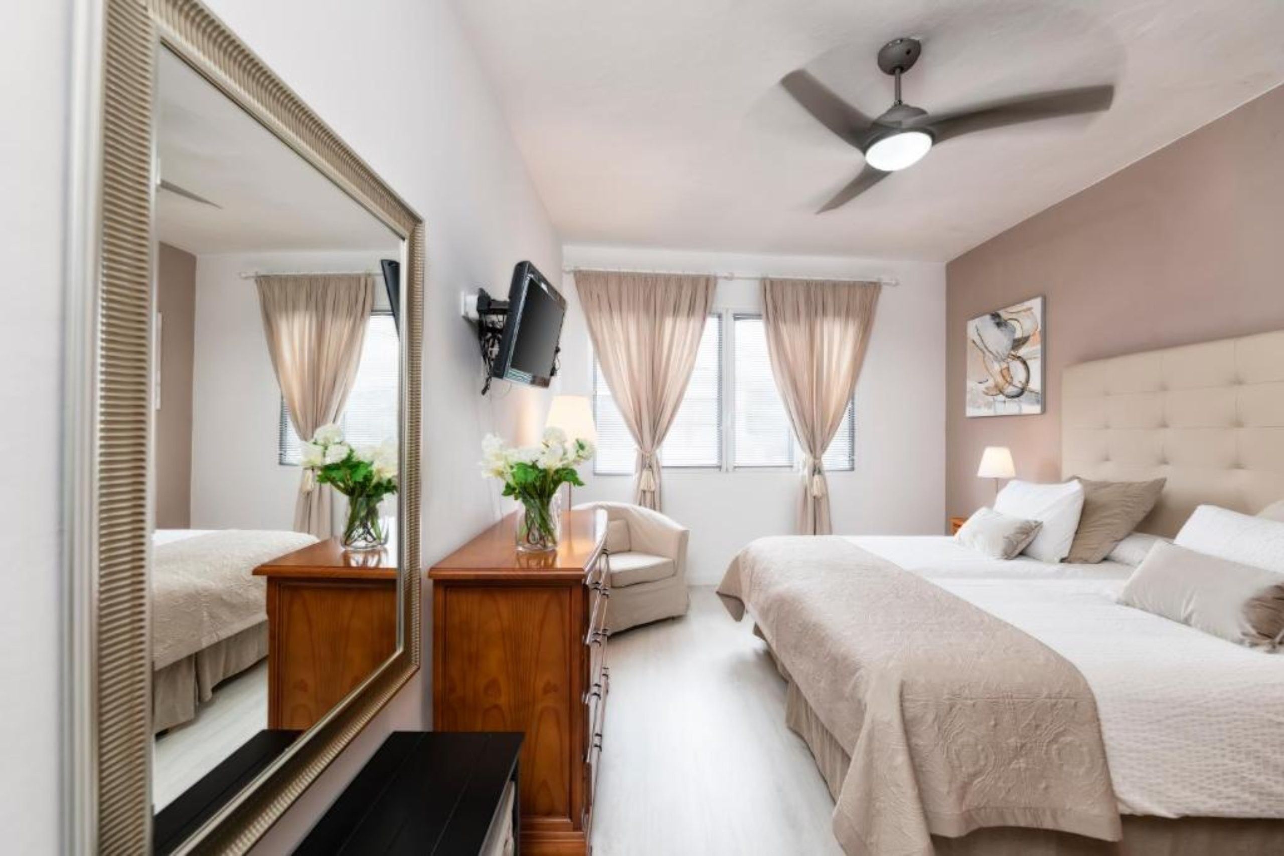 Une chambre d’hôtel équipée d’un lit, d’un bureau, d’une chaise, d’une télévision et d’un ventilateur de plafond.