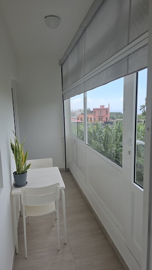 Un balcon avec une table et des chaises blanches, un pot de fleurs et une vue sur des immeubles et des arbres.
