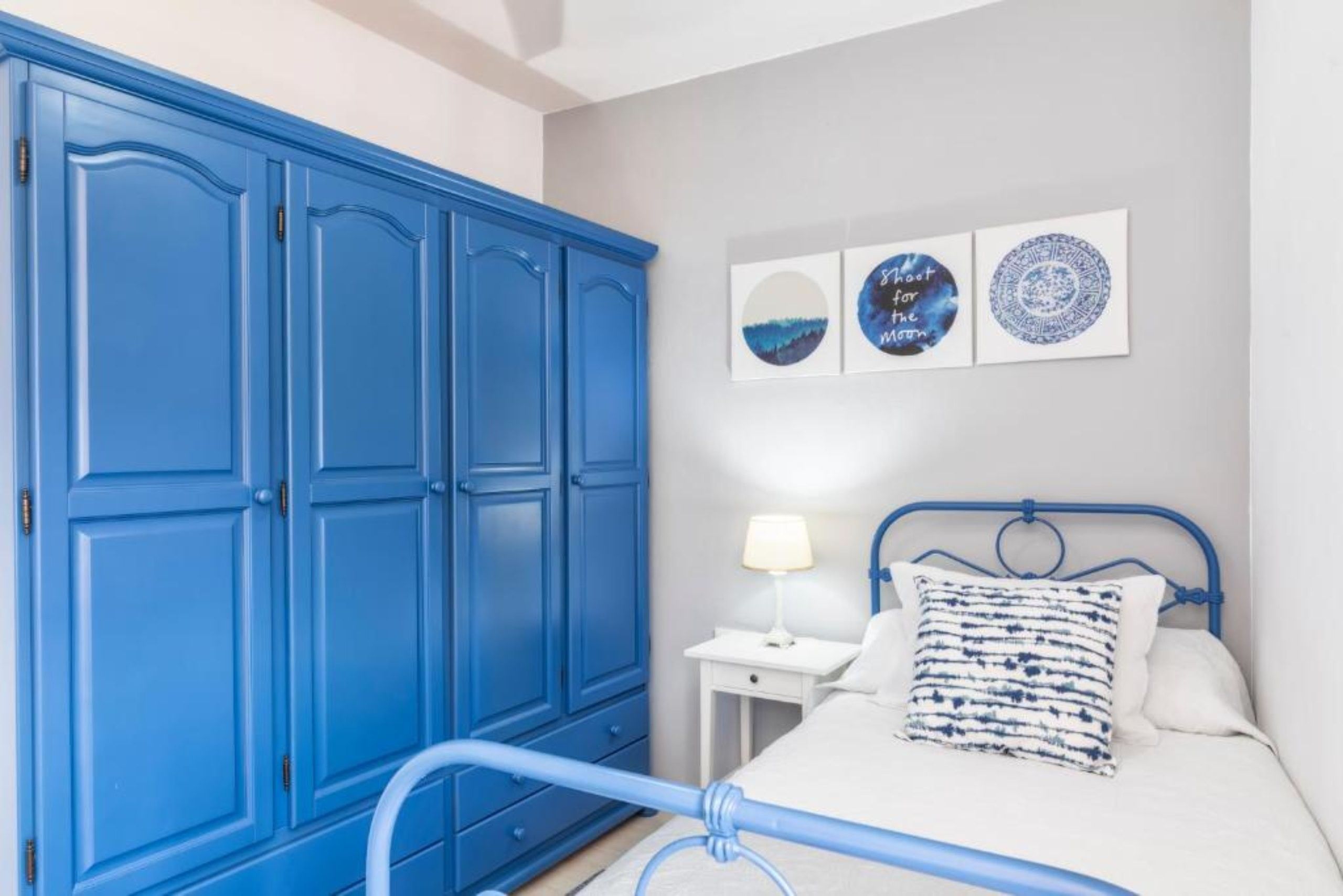 A bedroom with a bed, a nightstand, a blue wardrobe, and wall art.