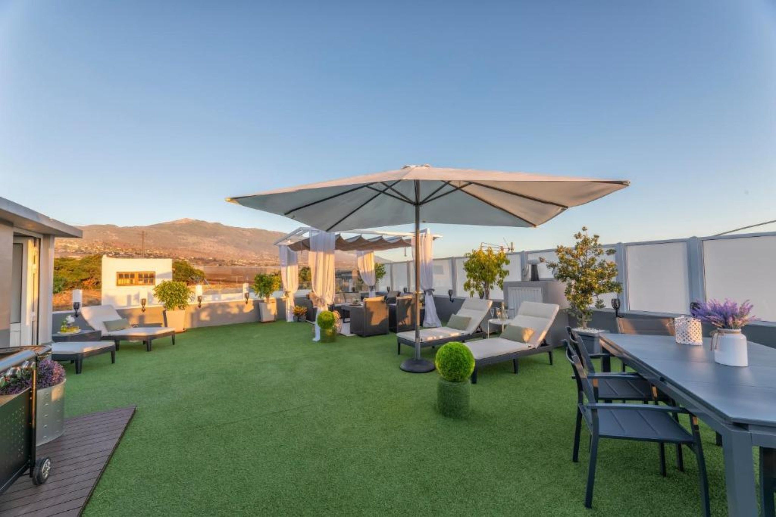 Een dakterras met kunstgras, tuinmeubilair en een grote parasol voor schaduw.