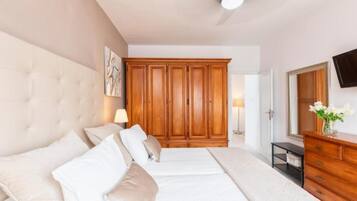 A bedroom with a large bed, a wardrobe, a dresser, a television, and a ceiling fan.