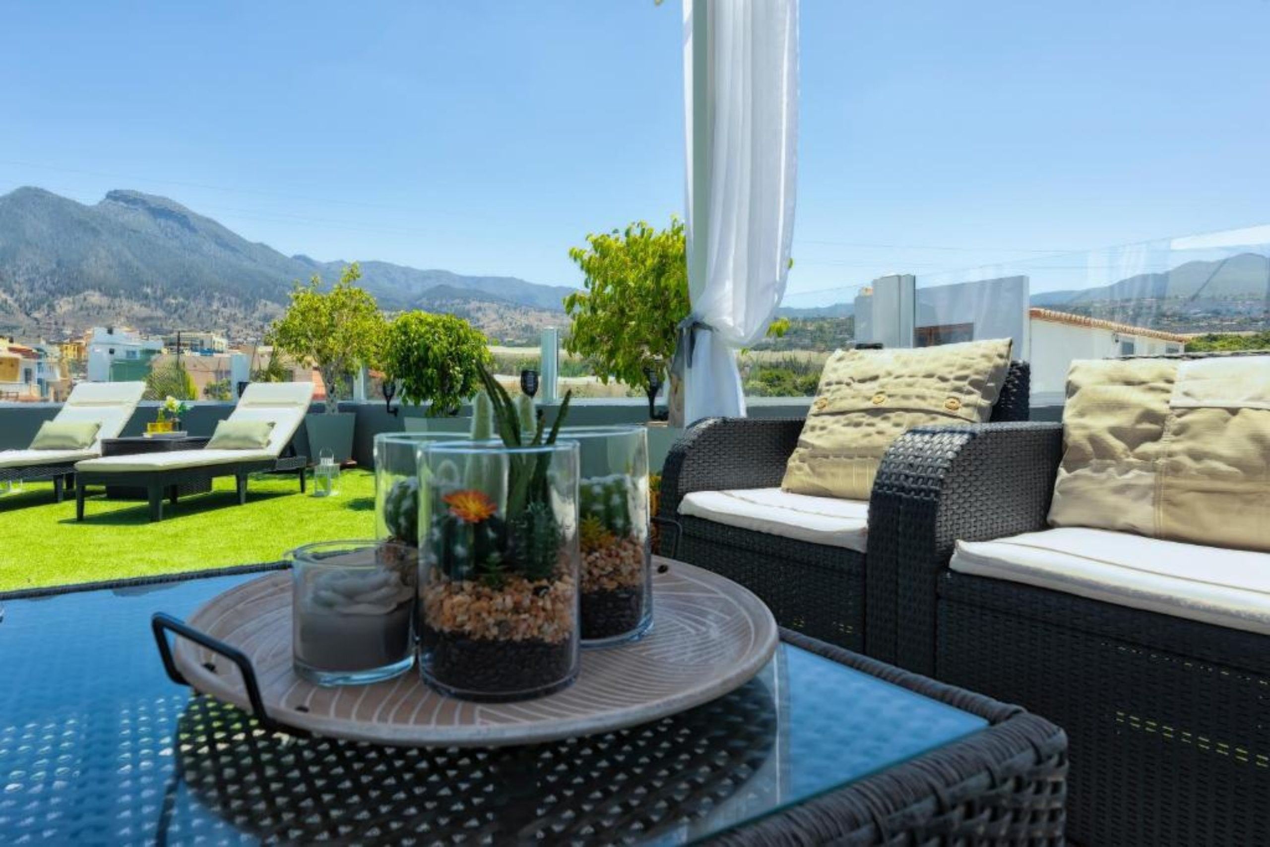 Une terrasse avec des sièges extérieurs, une table en verre et une vue sur les montagnes.