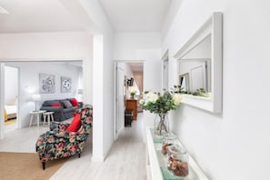 Een moderne woonkamer met een bank, een salontafel en een fauteuil met bloemenprint. Er is een gang die naar een andere kamer leidt.