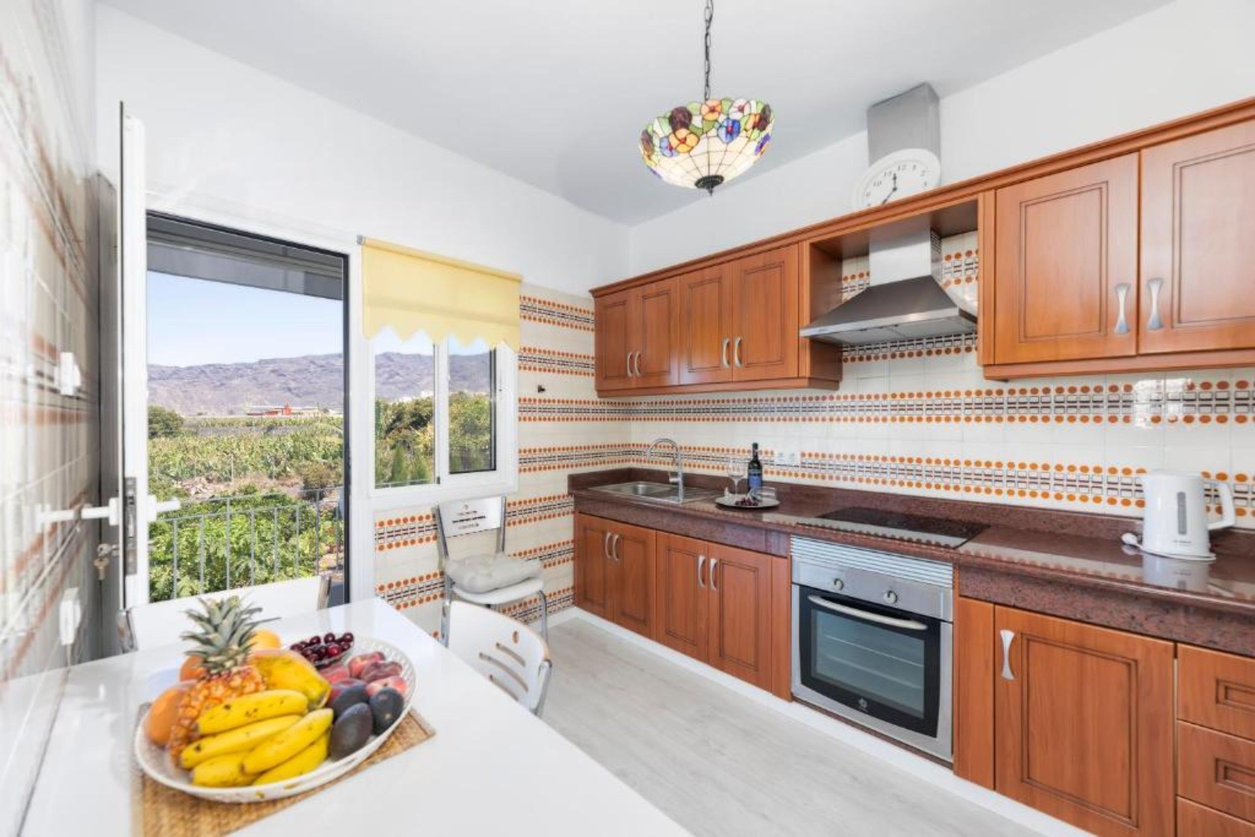 Une cuisine moderne avec des meubles en bois, un four en acier inoxydable et une grande fenêtre donnant sur un paysage montagneux.