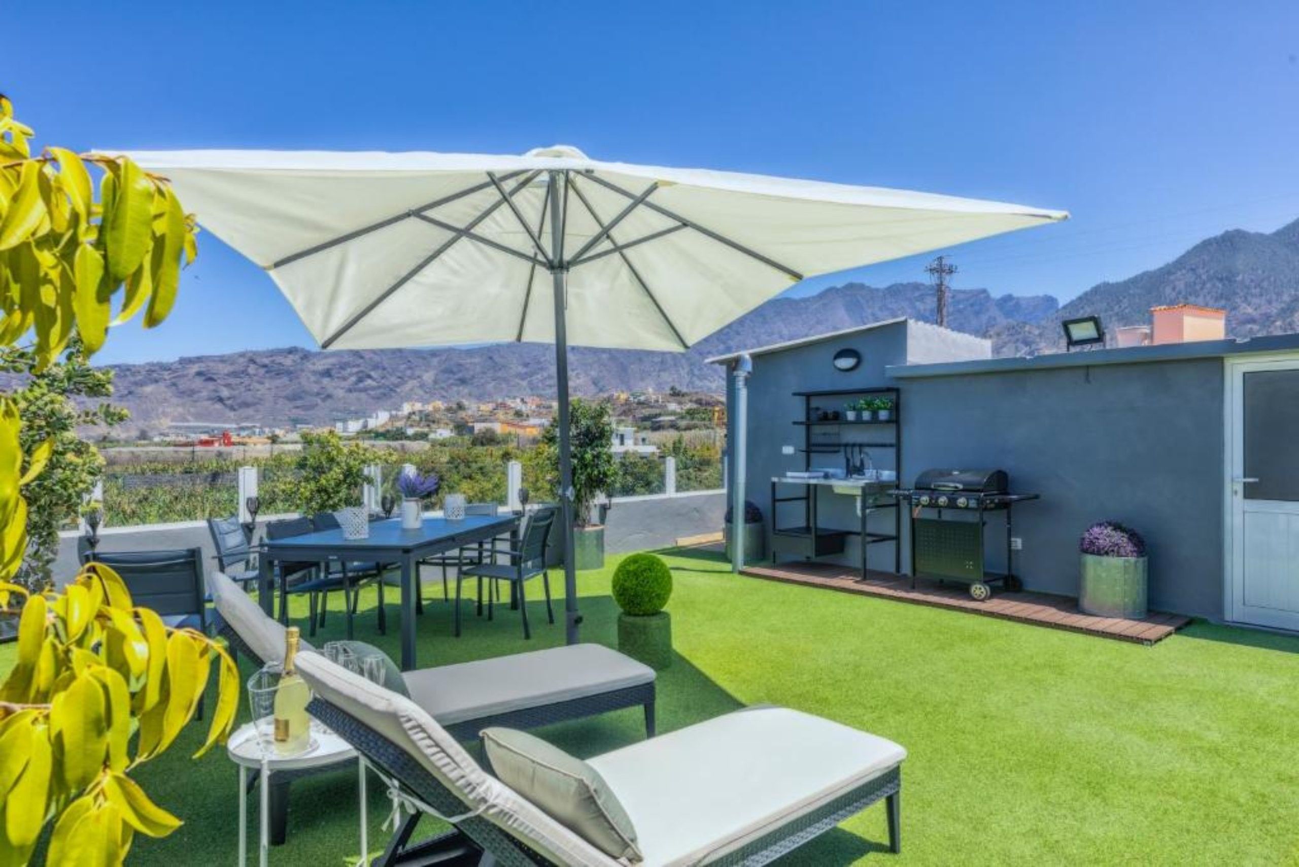 A patio with a table, chairs, a grill, and a view of the mountains.