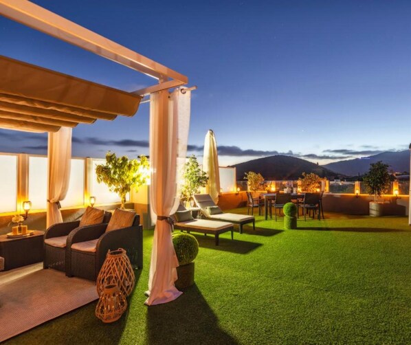 Un patio exterior con zona de comedor, sillones de descanso y vistas a las montañas.