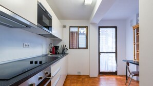 A compact kitchen with a stove, oven, and microwave. There is a window with blinds and a door leading to another room. - Vacation Apartment in Central Fuengirola with Balcony, Air Conditioning, and WiFi (Fuengirola)