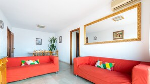A room with two red sofas, a wooden cabinet, a dining table with chairs, a potted plant, and a large mirror on the wall. - Vacation Apartment in Central Fuengirola with Balcony, Air Conditioning, and WiFi (Fuengirola)