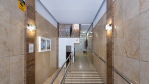 Un couloir au sol de marbre, doté de rampes, d’un mur orné de motifs et d’une porte au fond.