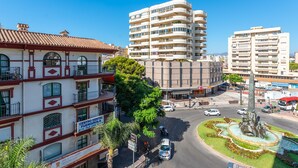 Un immeuble à plusieurs étages doté de balcons, d’une fontaine centrale et surplombant un ciel d’un bleu limpide.