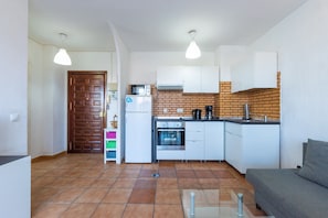 A compact kitchen with a microwave, oven, and coffee maker, a wooden door, and a grey sofa.