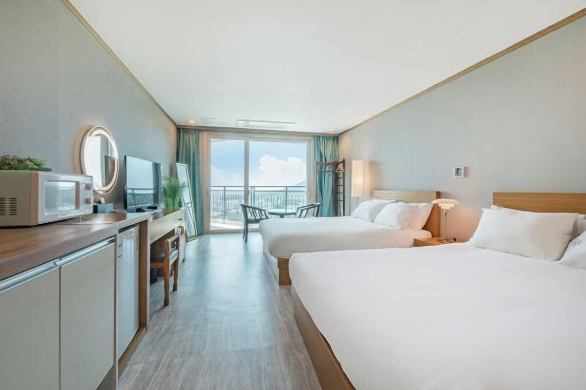 Ein Hotelzimmer mit zwei Betten, einer Küchenzeile, einem Fernseher und einem Balkon mit Blick.